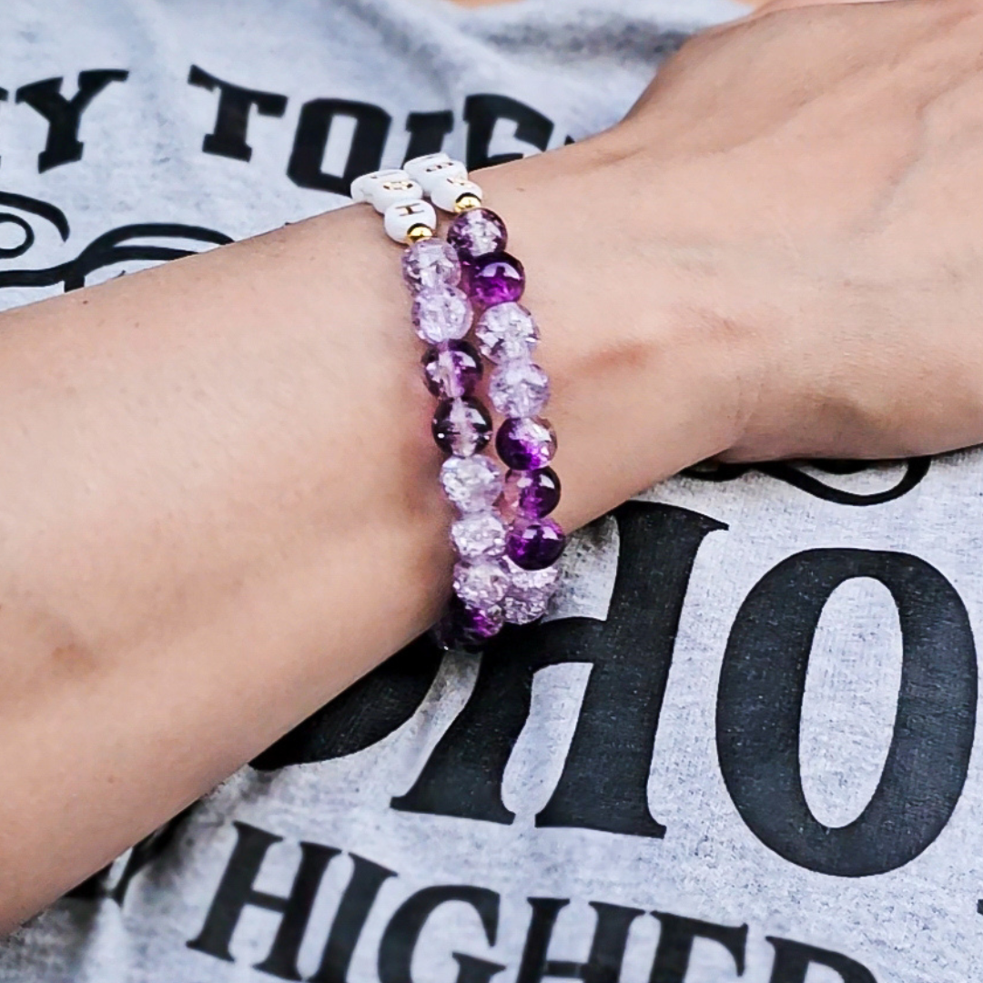 Person wearing a bracelet with purple and white beads on a gray shirt background