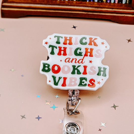 Retractable badge holder featuring the phrase “Thick Thighs and Bookish Vibes” in colorful retro lettering, ideal for book lovers, teachers, and nurses.