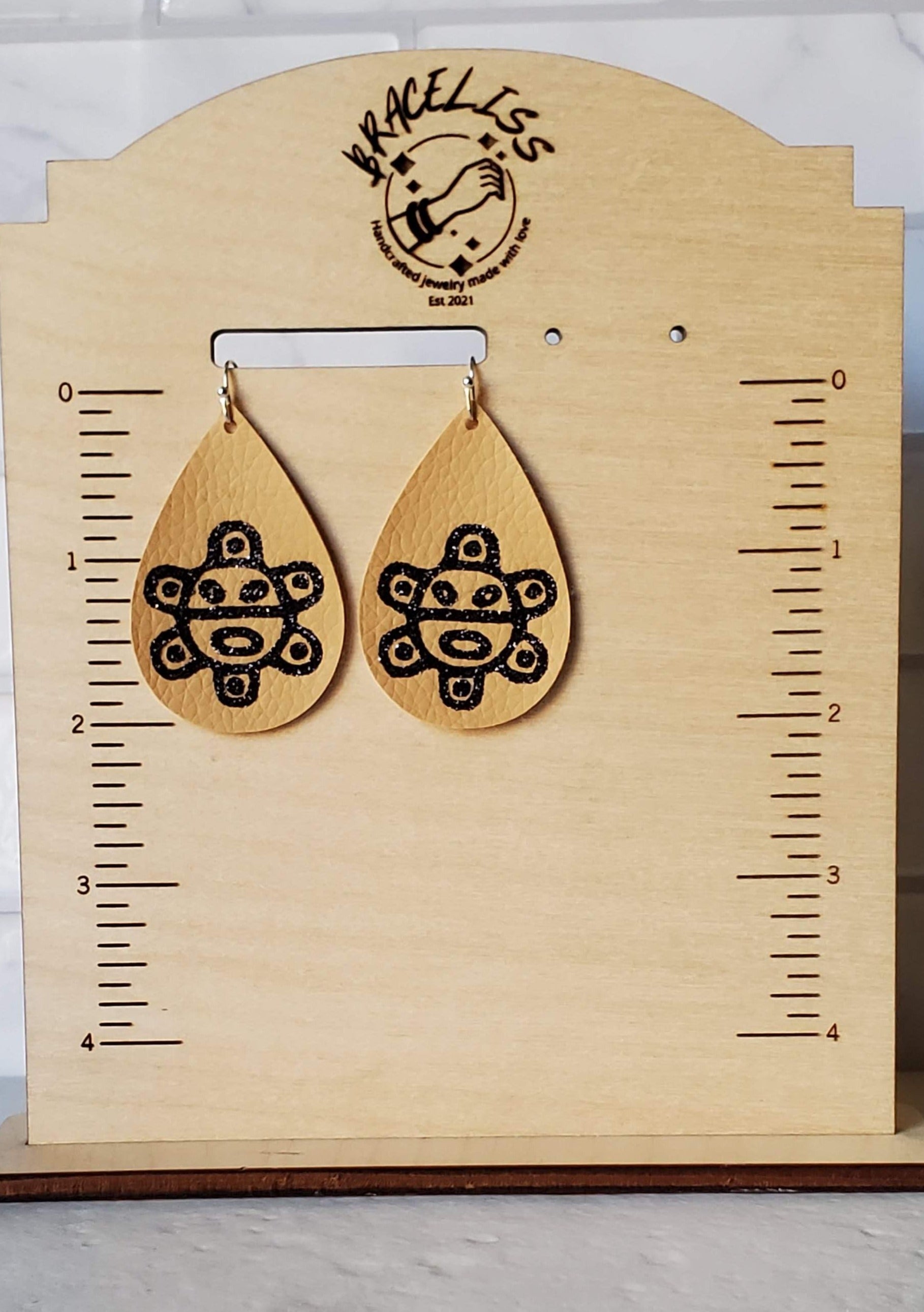 Taino sol earrings - Brown faux leather earrings on measuring display - braceliss