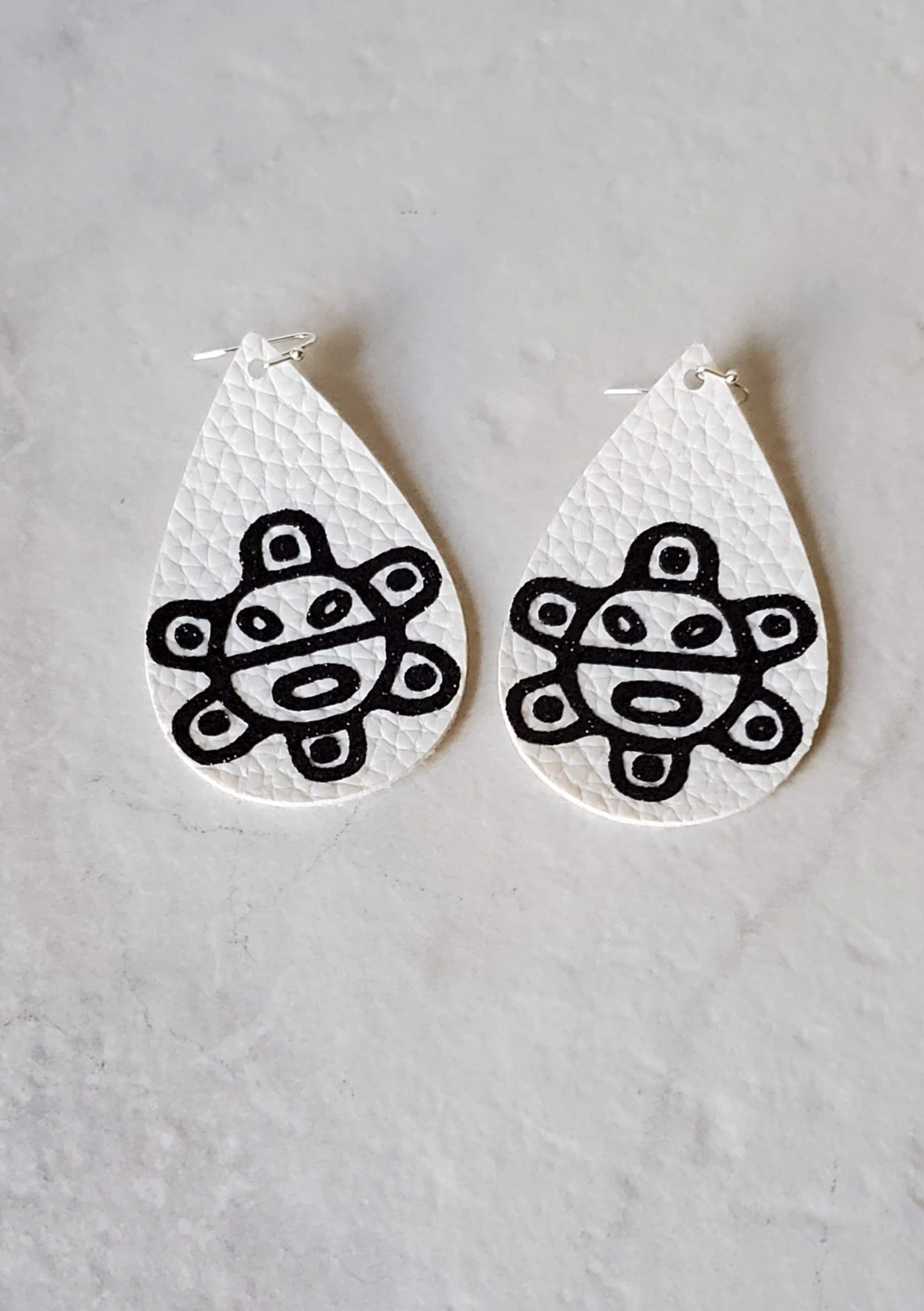 Taino sol earrings - white faux leather earrings laying flat - braceliss