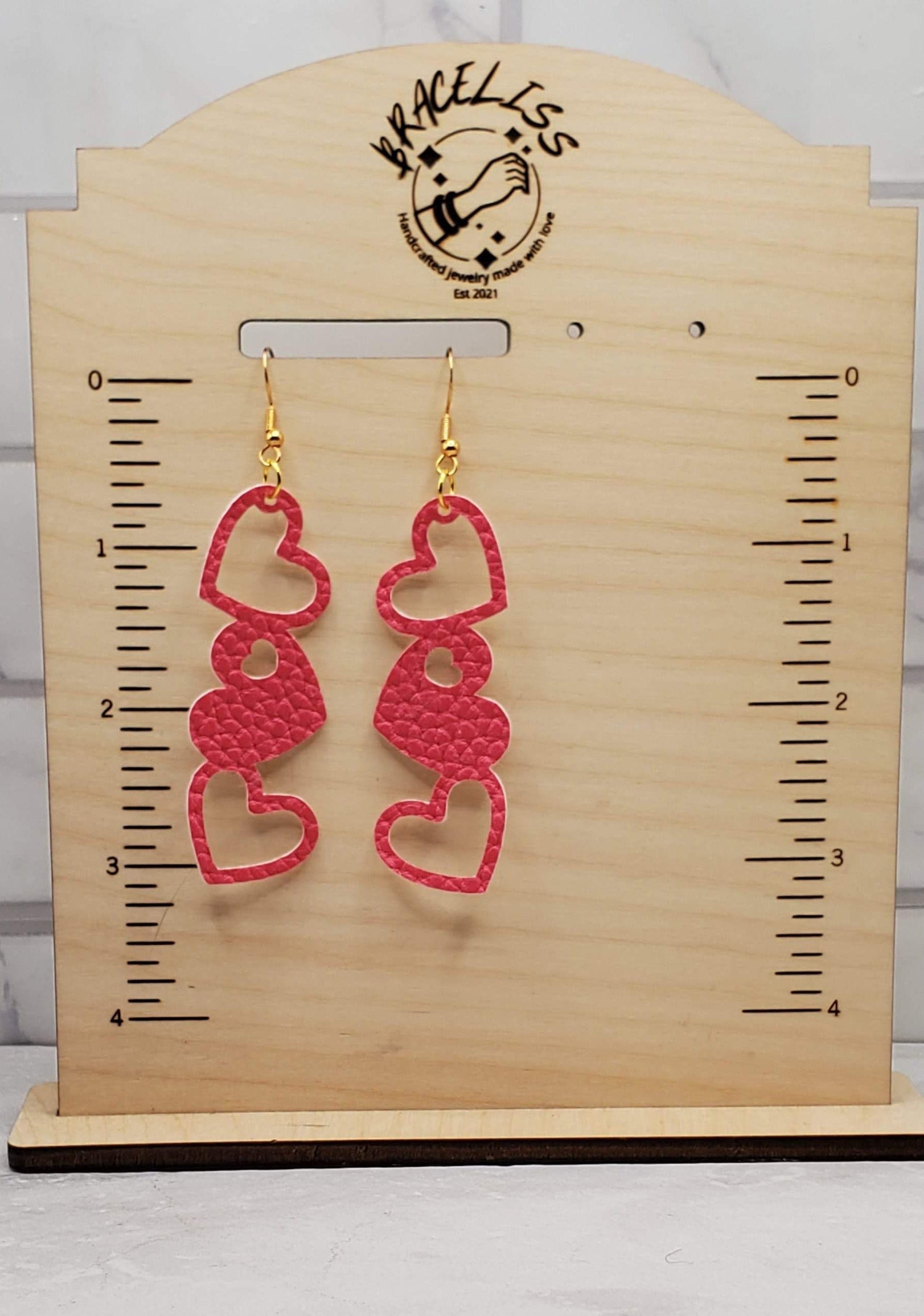 Hollow heart trio | dark pink faux leather drop earrings on measuring display | Braceliss