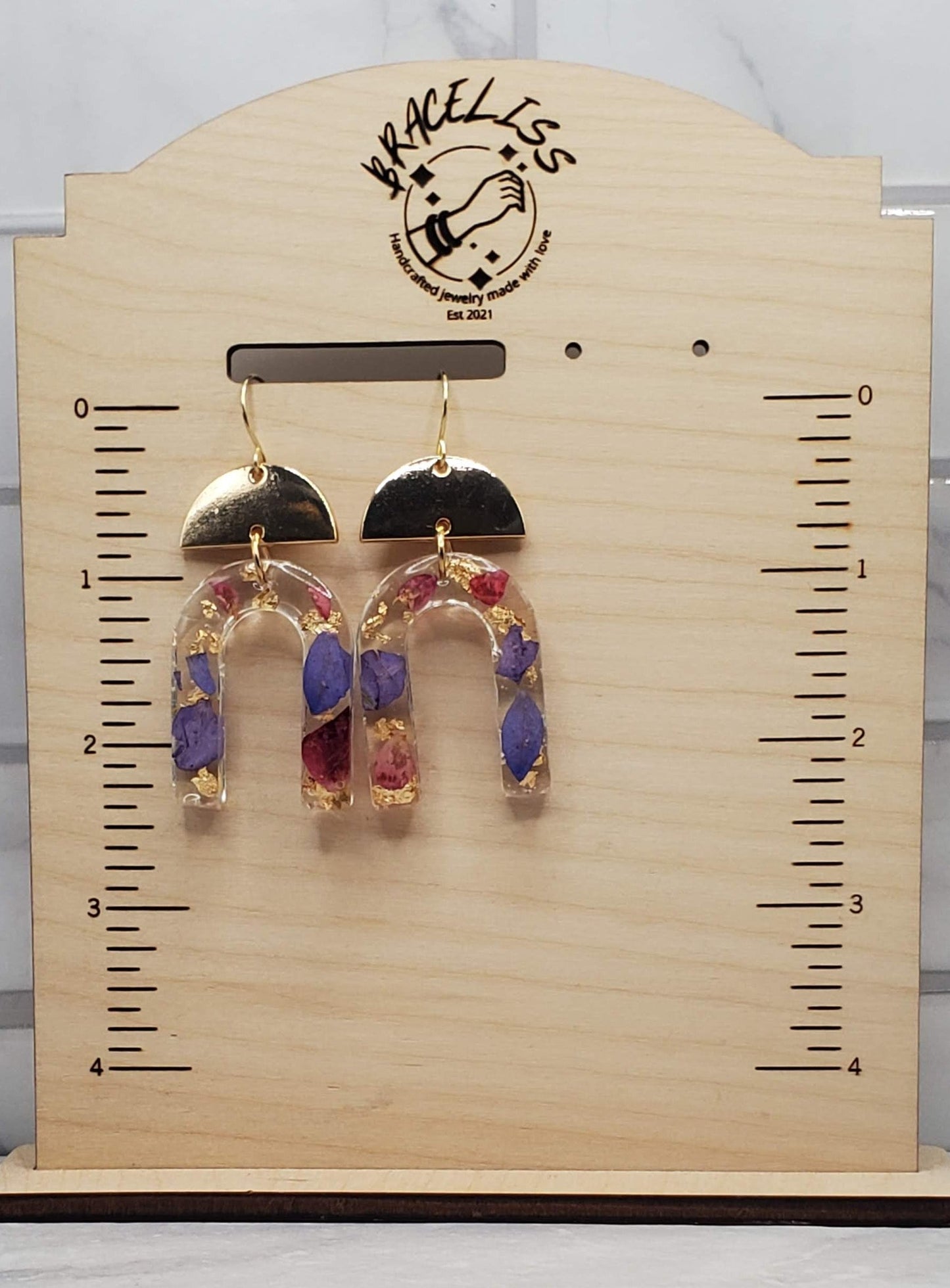Purple floral arch earrings | pressed flower resin earrings on measuring display | Braceliss